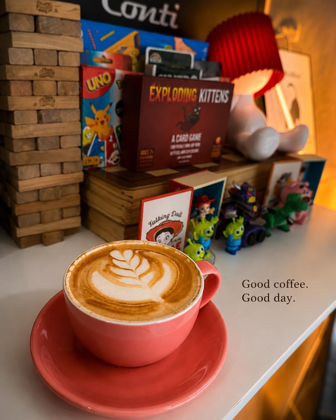 A latte in a red cup beside board games and playful shelf decorations.