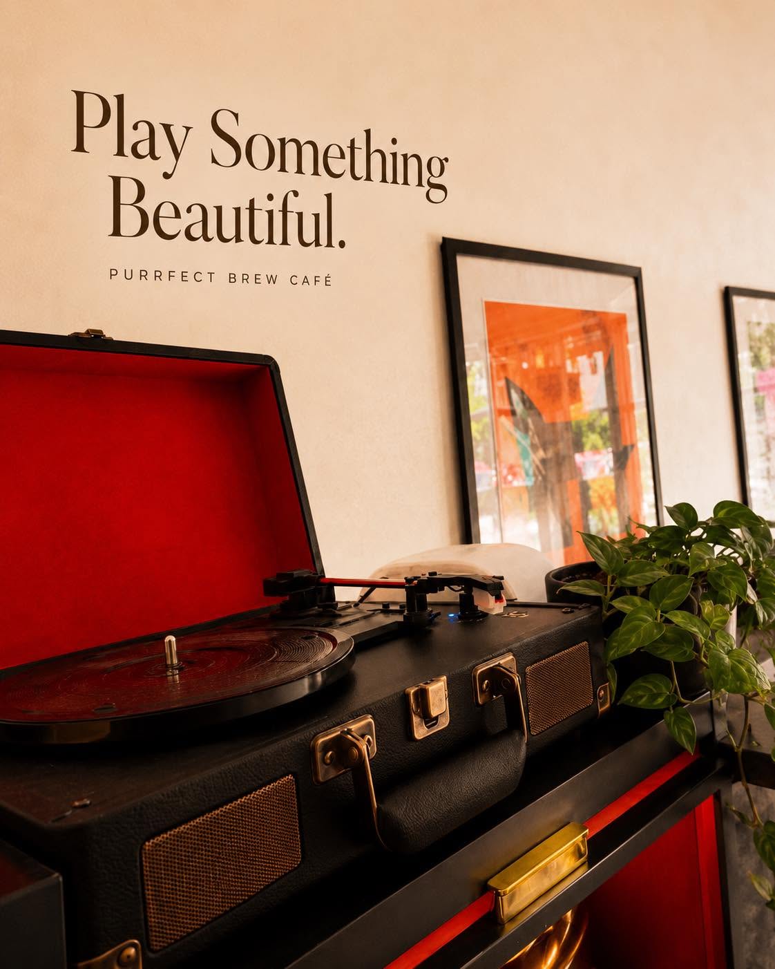A record player in a vintage suitcase beside framed art and plants.