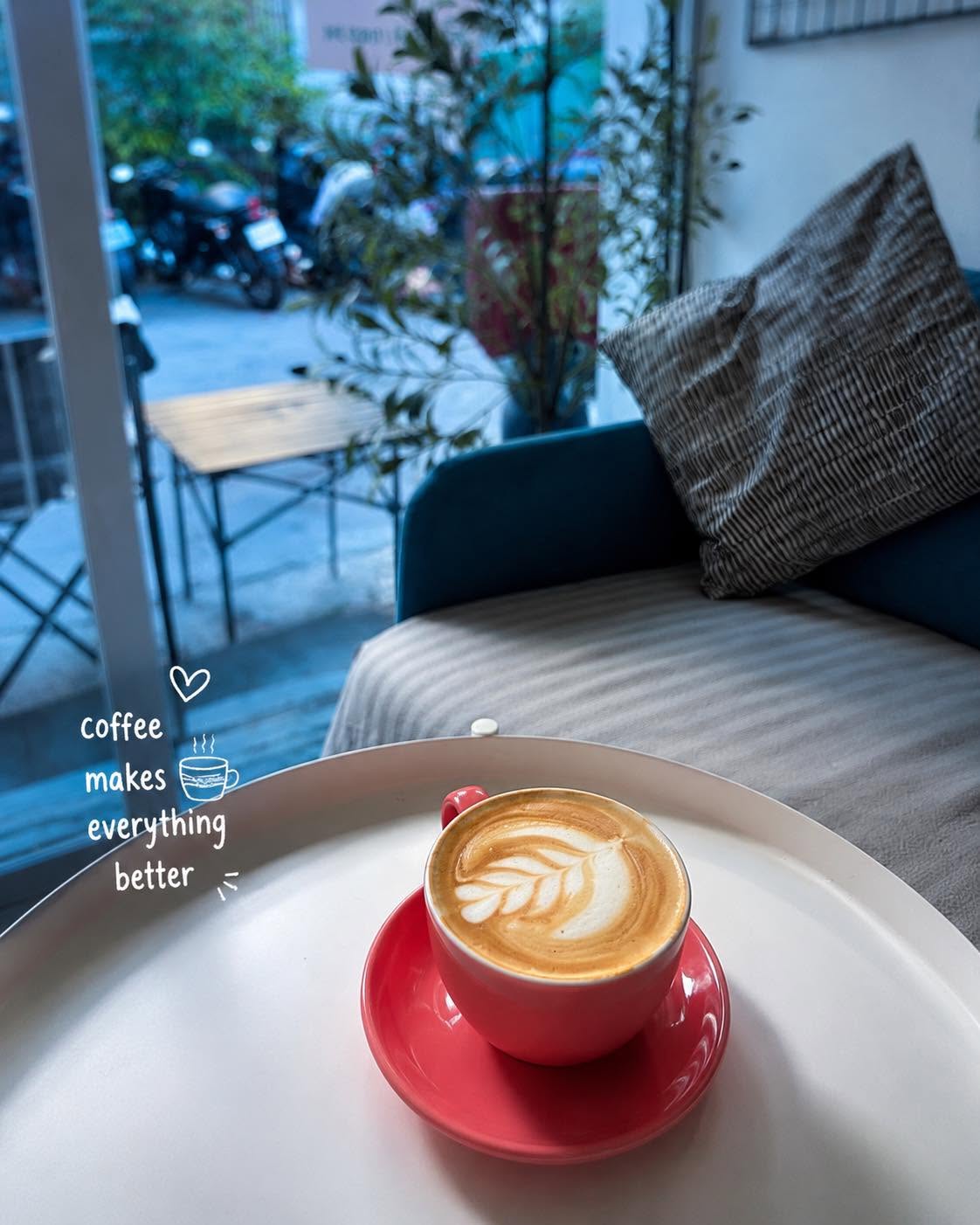 A latte on a white table beside cushioned window seating.